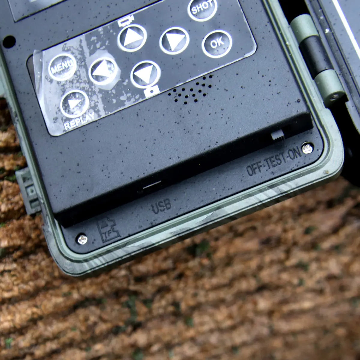 Close-up of trail camera controls with menu, shot, replay, and navigation buttons.