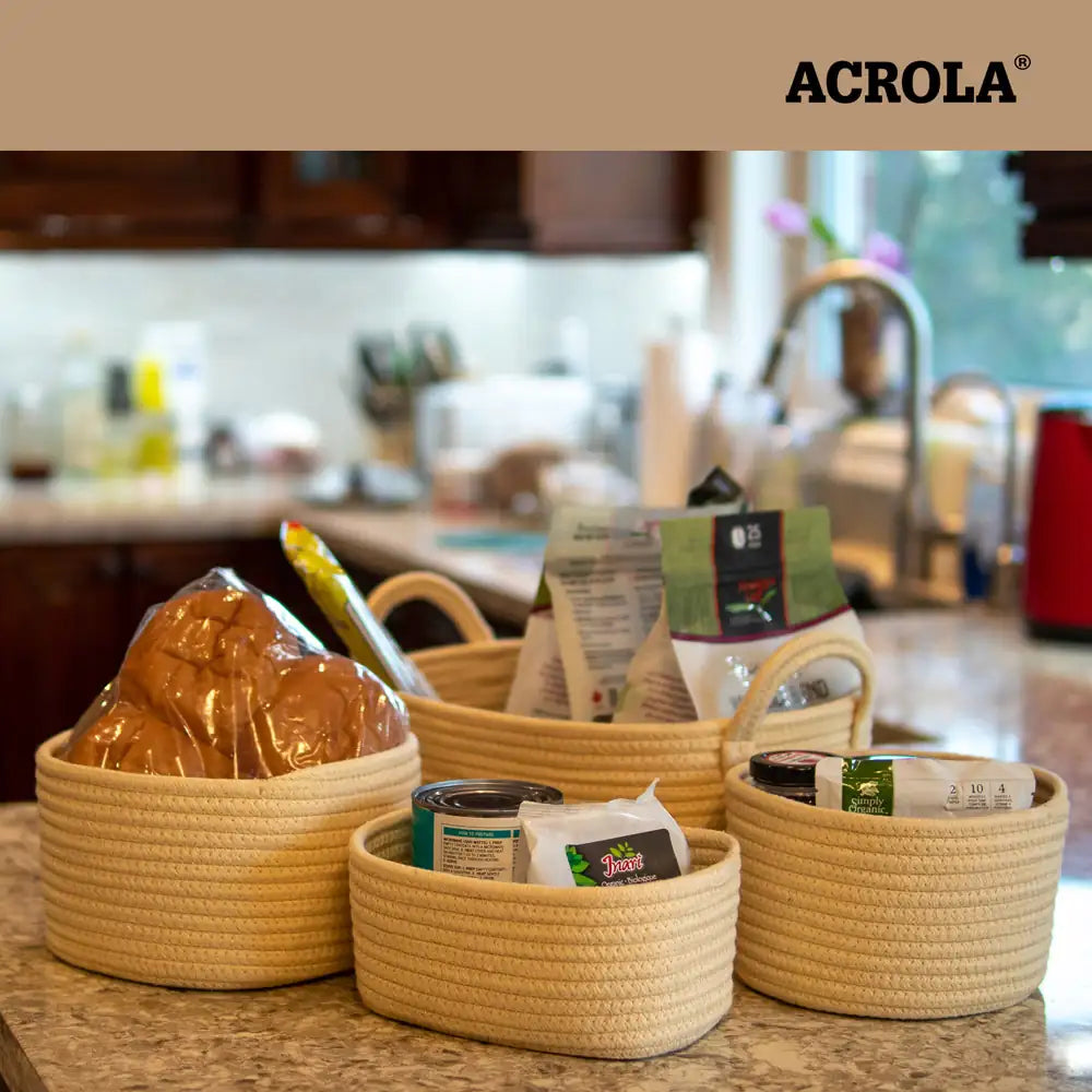 Woven baskets on a kitchen counter with various items, featuring the Acrola brand.