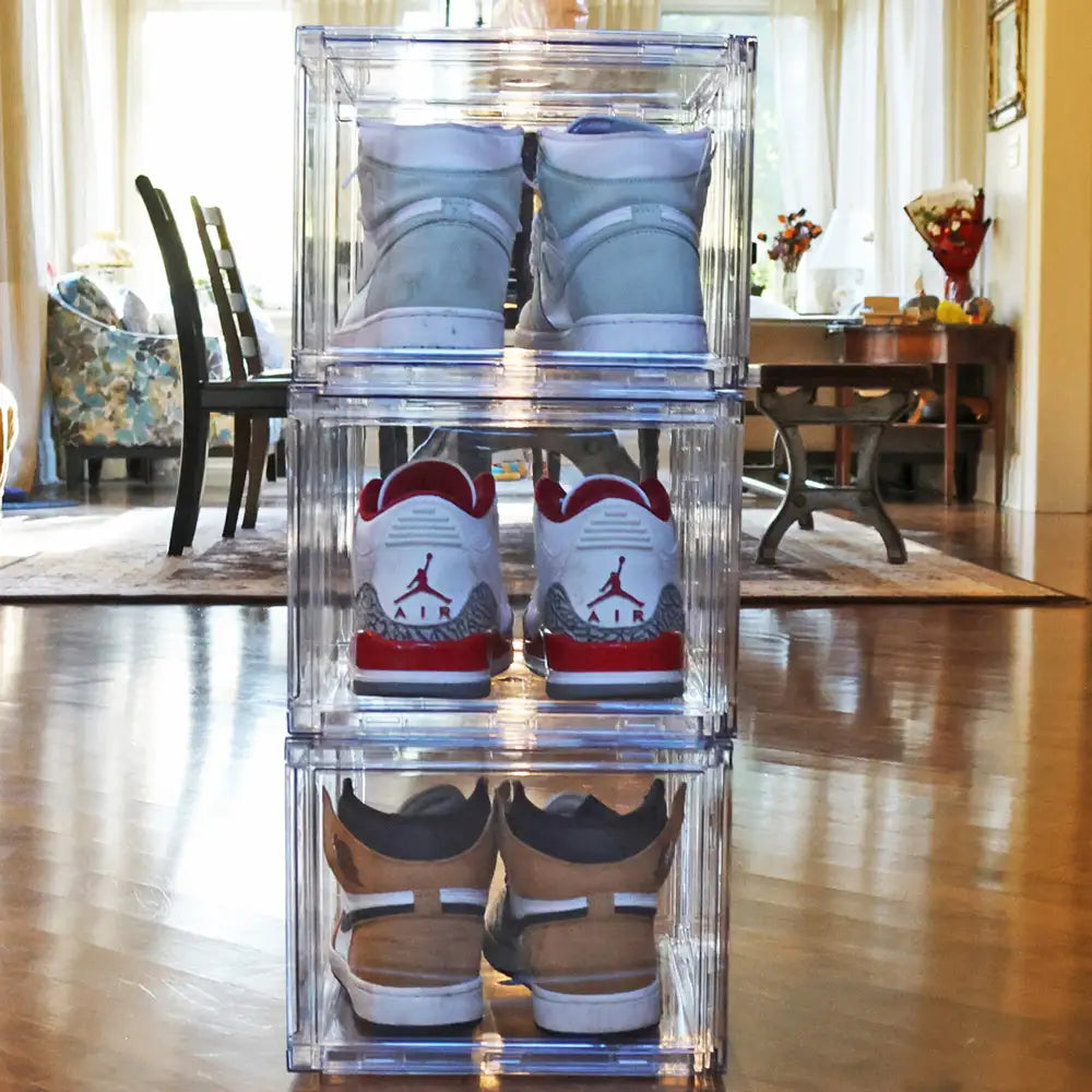 Stack of clear shoe boxes containing sneakers on a wooden floor.