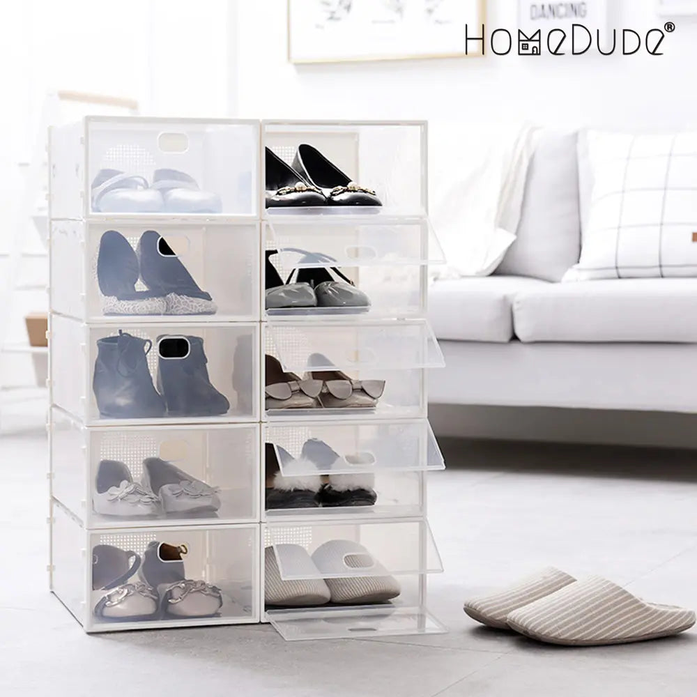 Clear shoe storage boxes with shoes inside, placed on a light-colored floor with a white sofa in the background.