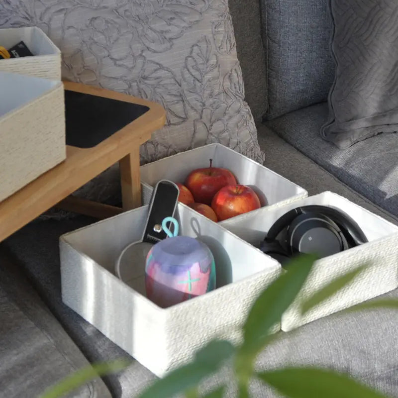 White storage bin with items including apples and a pink container on a gray couch.