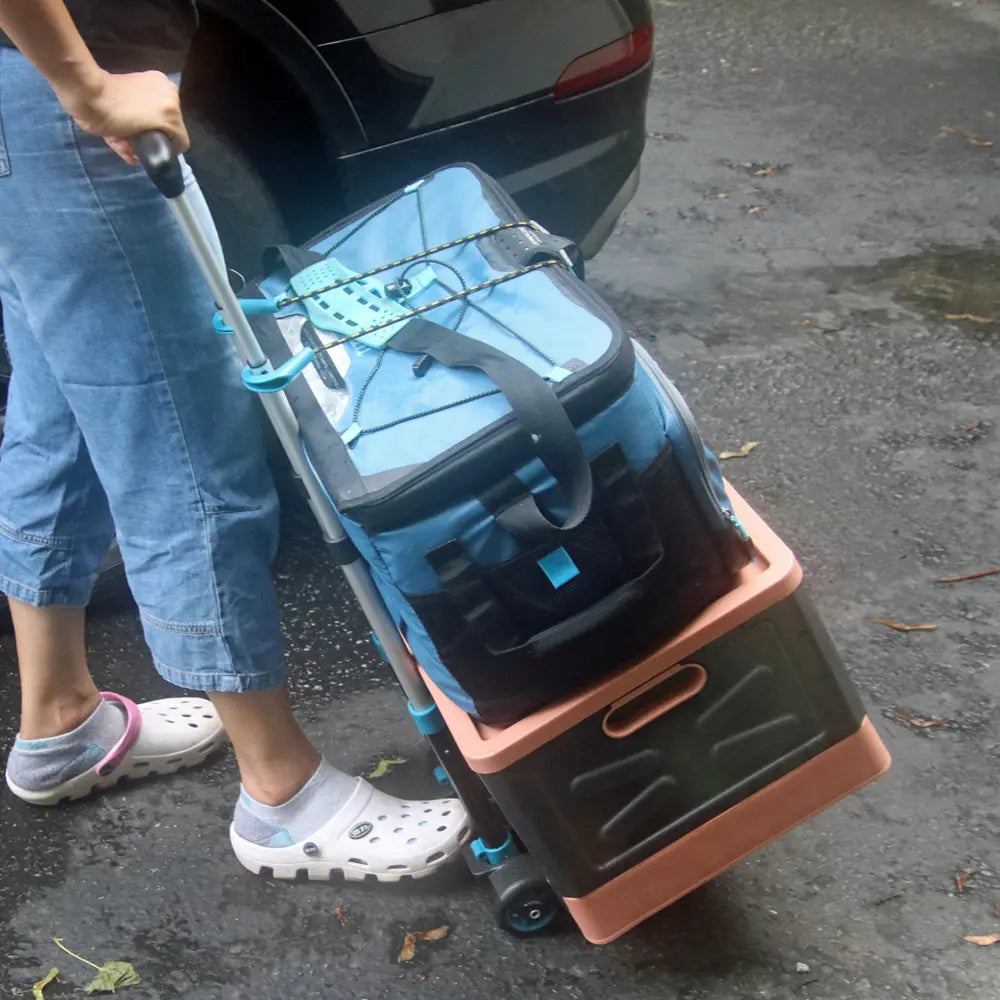 Person using a wheeled cooler box to load items into a car trunk.