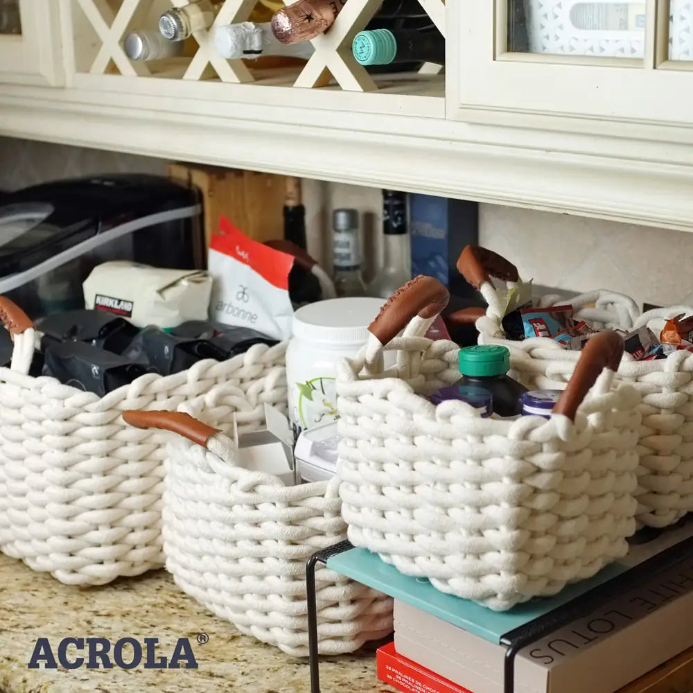 White woven baskets with handles on a kitchen counter, containing various items, with 'ACROLA' branding visible.