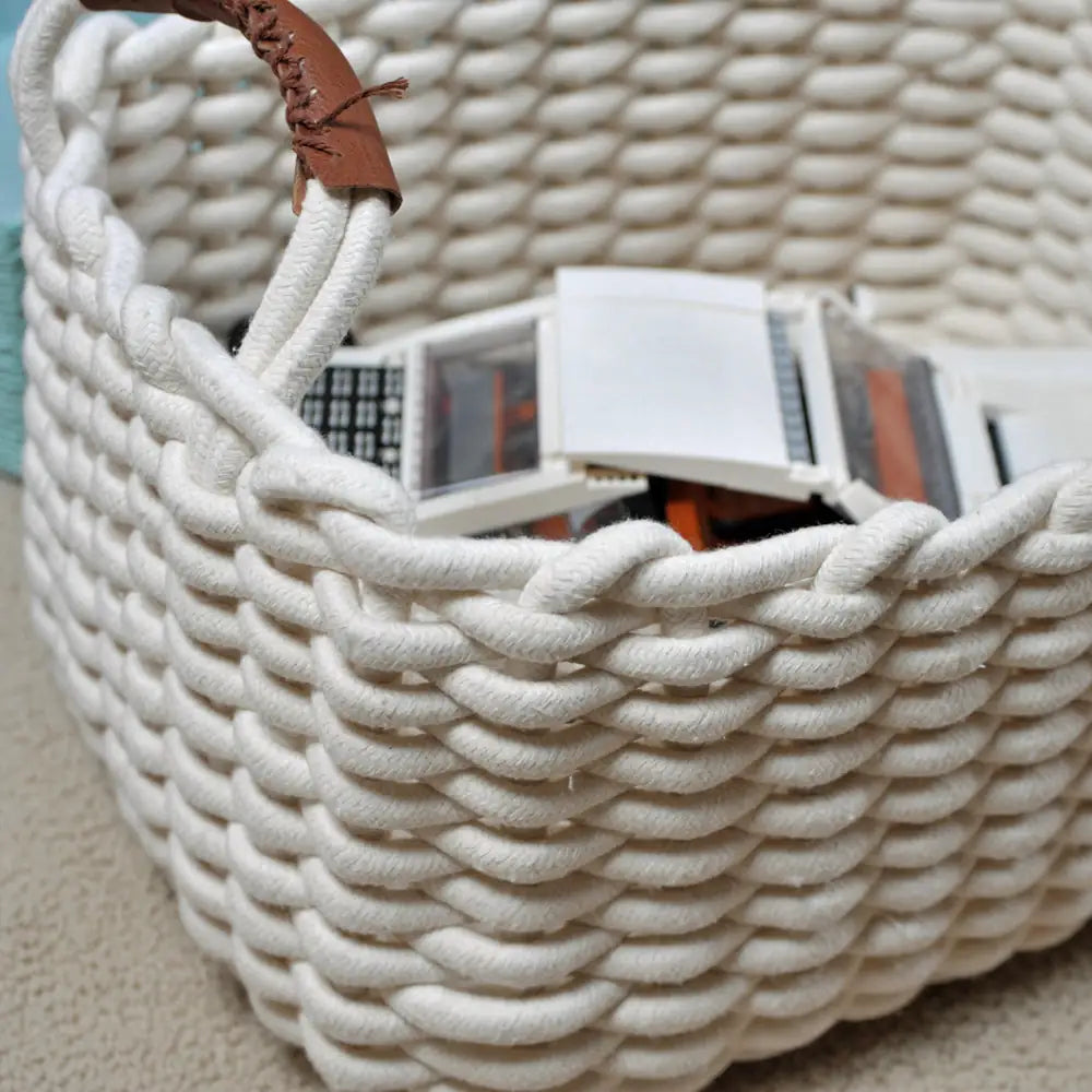 White woven basket with a brown handle containing books on a light background