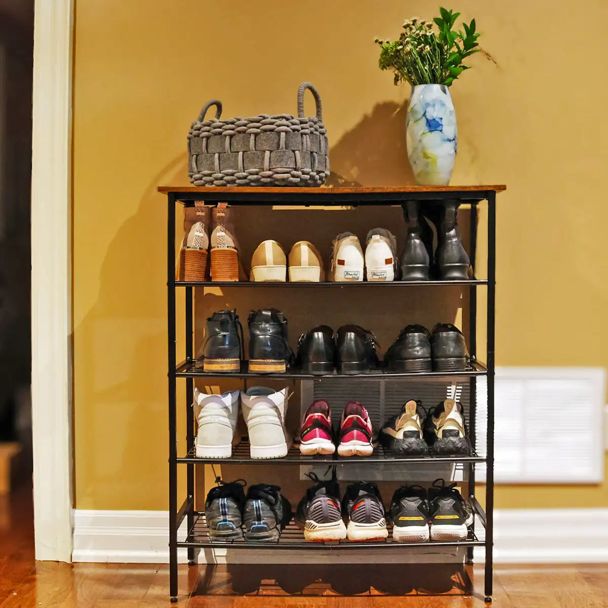 Shoe rack with various shoes on a wooden floor against a yellow wall.